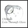Close-up image of a hand holding a glass with a coin visibly embedded into its side, showcasing the Ultimate Coin Thru Glass magic trick effect from SEO Magic.