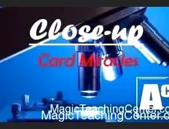 A close-up shot of a magician's hands demonstrating an easy card trick, holding a deck of playing cards, with a blurred background suggesting an audience or performance setting.